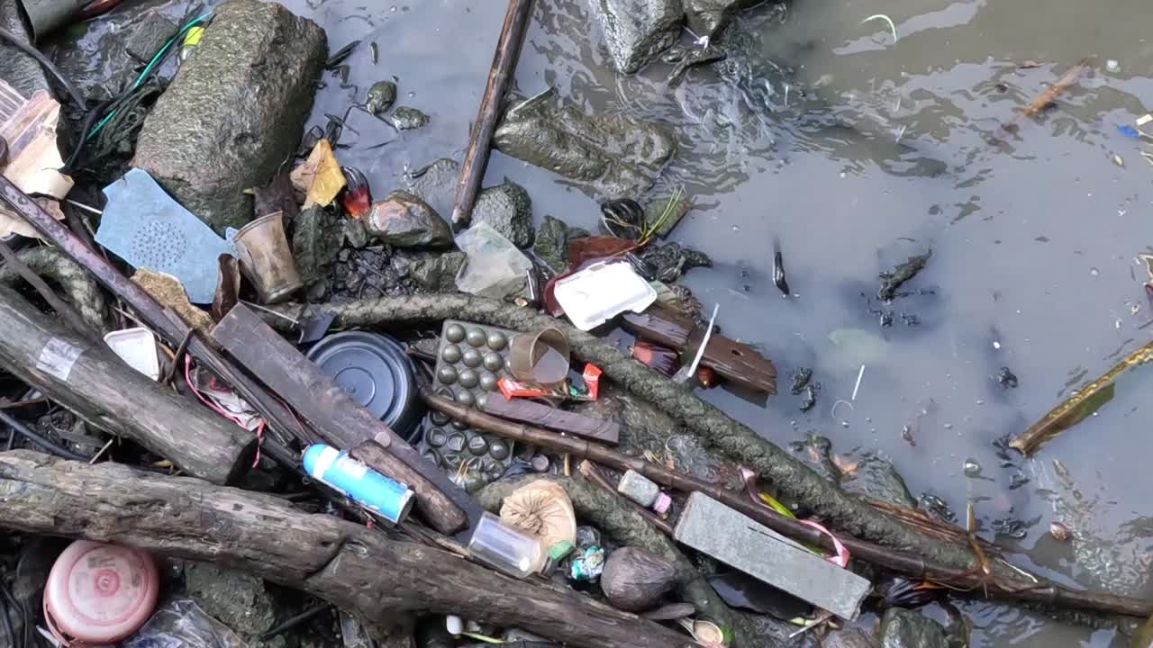 Close-up view of various debris floating in murky water, including plastic bottles and packaging.