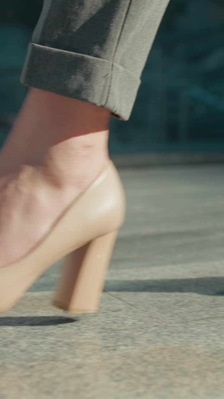 Close up side leg view of elegant lady walking gracefully in nude high heels along modern urban walkway with sunlight reflecting off glass building