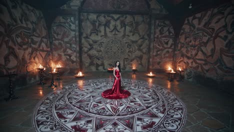woman wearing an elegant red dress stands on a large, ornate mandala in the center of an ancient temple, surrounded by burning torches, creating a mystical and spiritual atmosphere