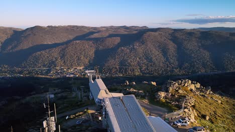 Revelación-Aérea-Inclinada-Del-Telesilla-De-Pista-De-Esquí-Vacía-En-Verano-Con-La-Ciudad-De-Thredbo-Al-Fondo,-Montañas-Nevadas,-Nueva-Gales-Del-Sur,-Australia