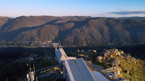 revelación aérea de la inclinación de la pendiente de esquí vacía en verano con la ciudad de thredbo en el fondo, montañas nevadas, nsw, australia