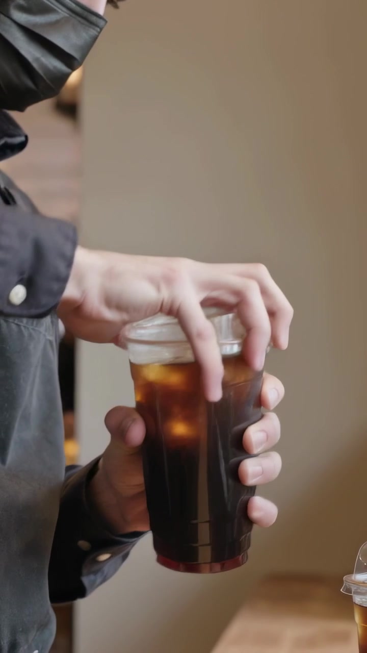 Video verticale: Barista con grembiule e mascherina che sistema il coperchio e poi consegna la tazza per il ritiro, con una cupola nelle vicinanze
