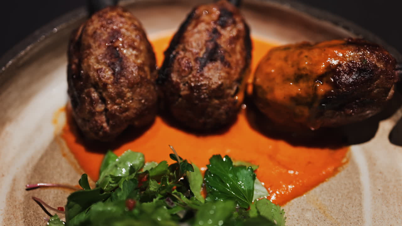 Three grilled meat skewers on charcoal sticks served on a plate with an orange sauce