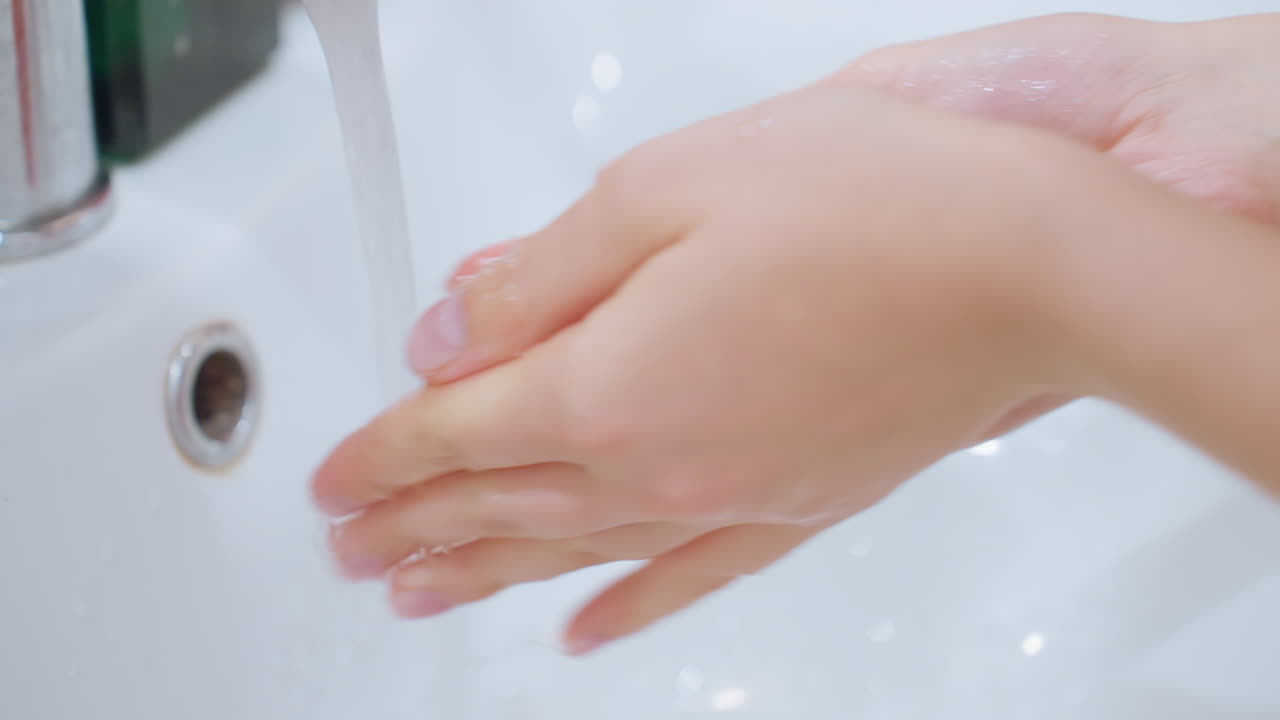 Close-up of hands washing under running tap, water flowing over hands, focus on hand hygiene and cleansing process, perfect for illustrating cleanliness, personal care, and water