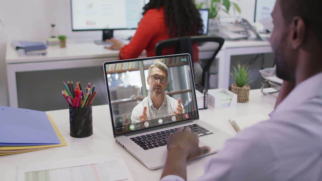 Video of african american man having video call on laptop with caucasian male coworker