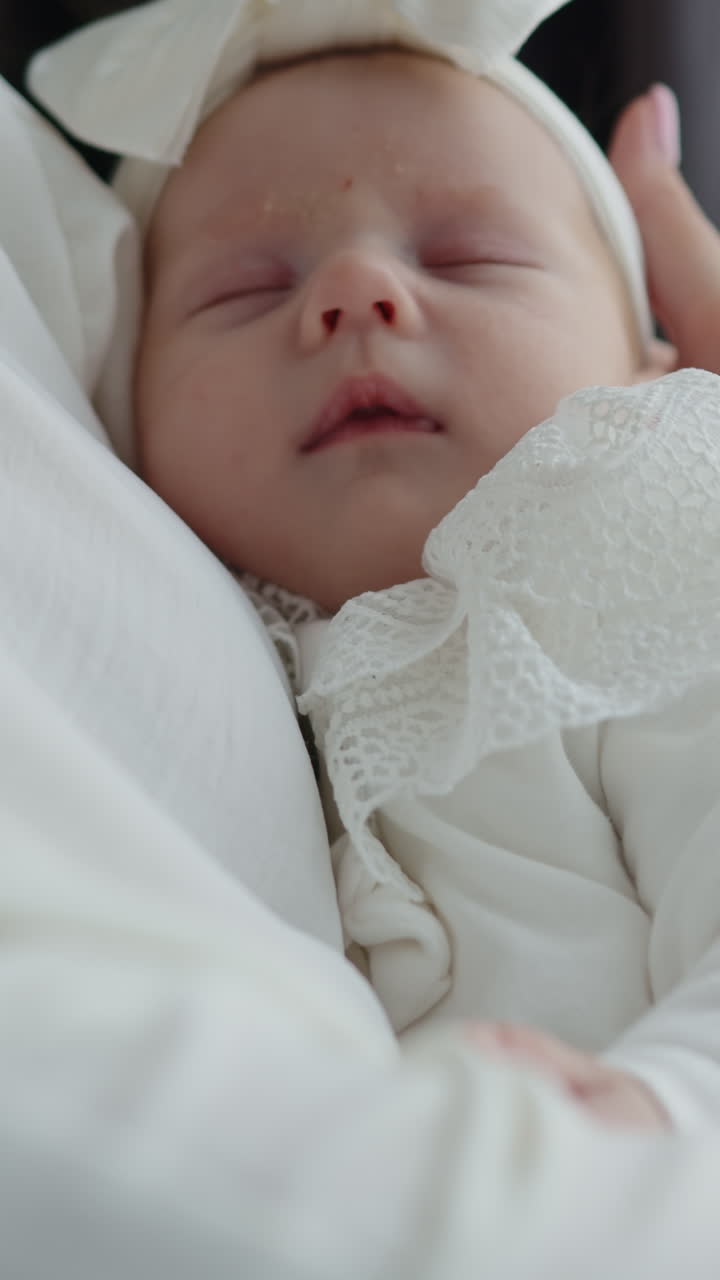 Primo piano di una neonata che dorme profondamente, avvolta in un tessuto bianco con un fiocco delicato