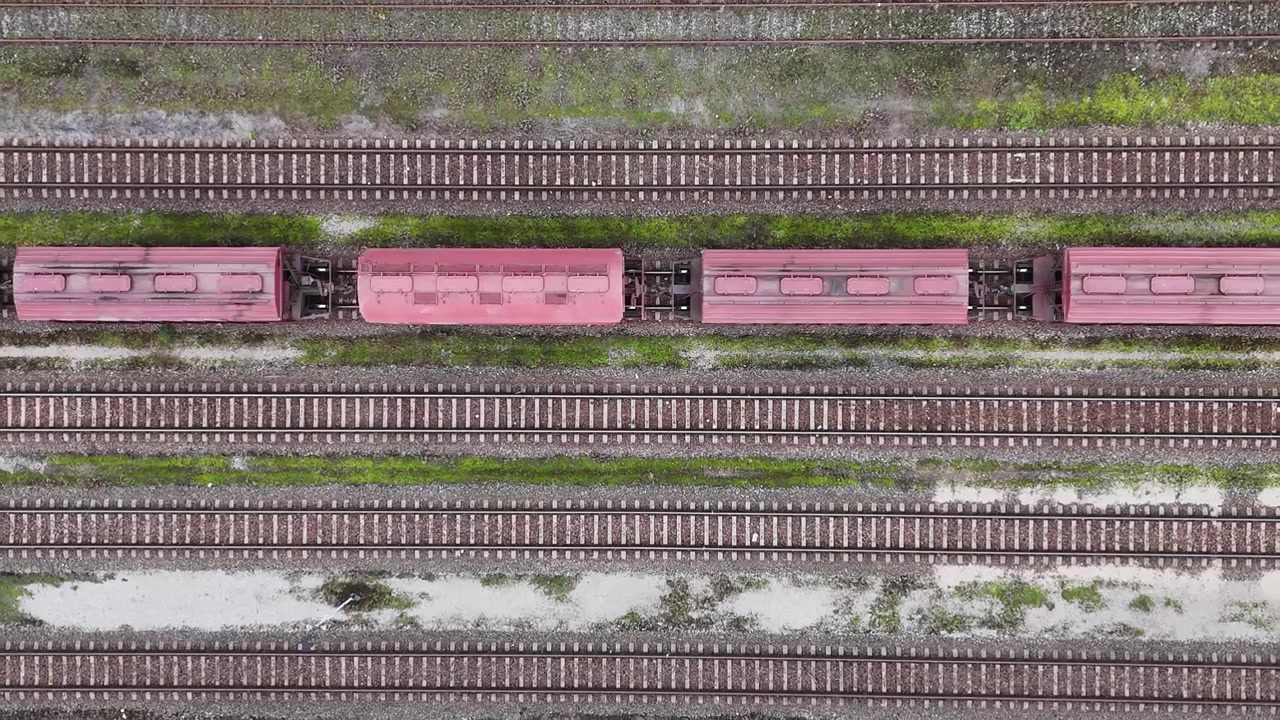 Rødt tog kører langs jernbanespor i et luftfoto på en overskyet dag.