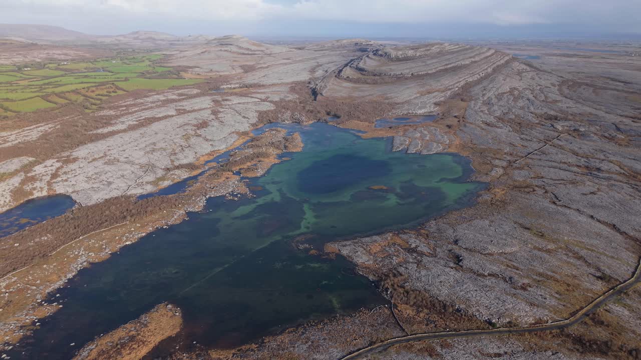 The Burren, County Clare, Ireland - A Scenic View of Rugged Limestone Terrain, Dark Lake Waters, and Distant Farmland - Aerial Drone Shot