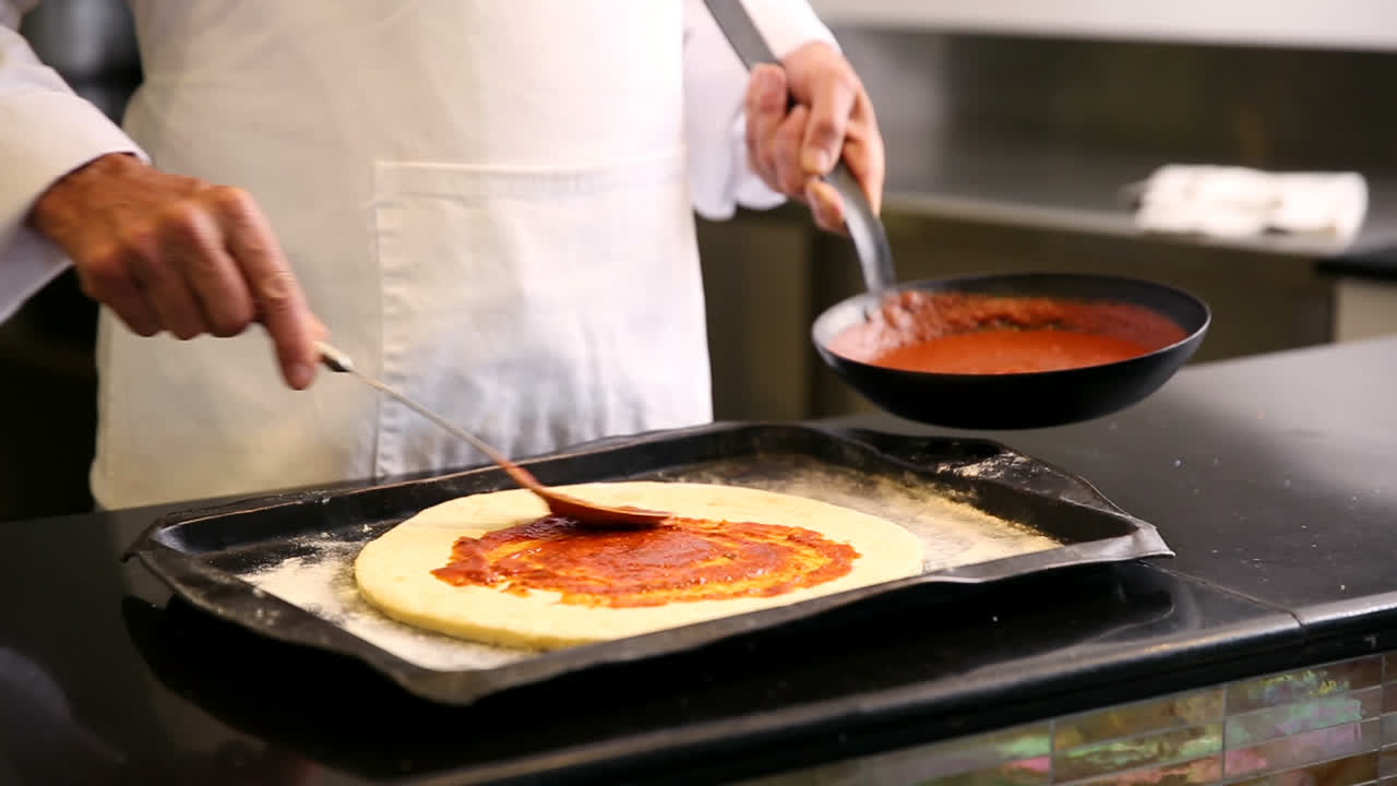 Kokk sprer saus på en pizza