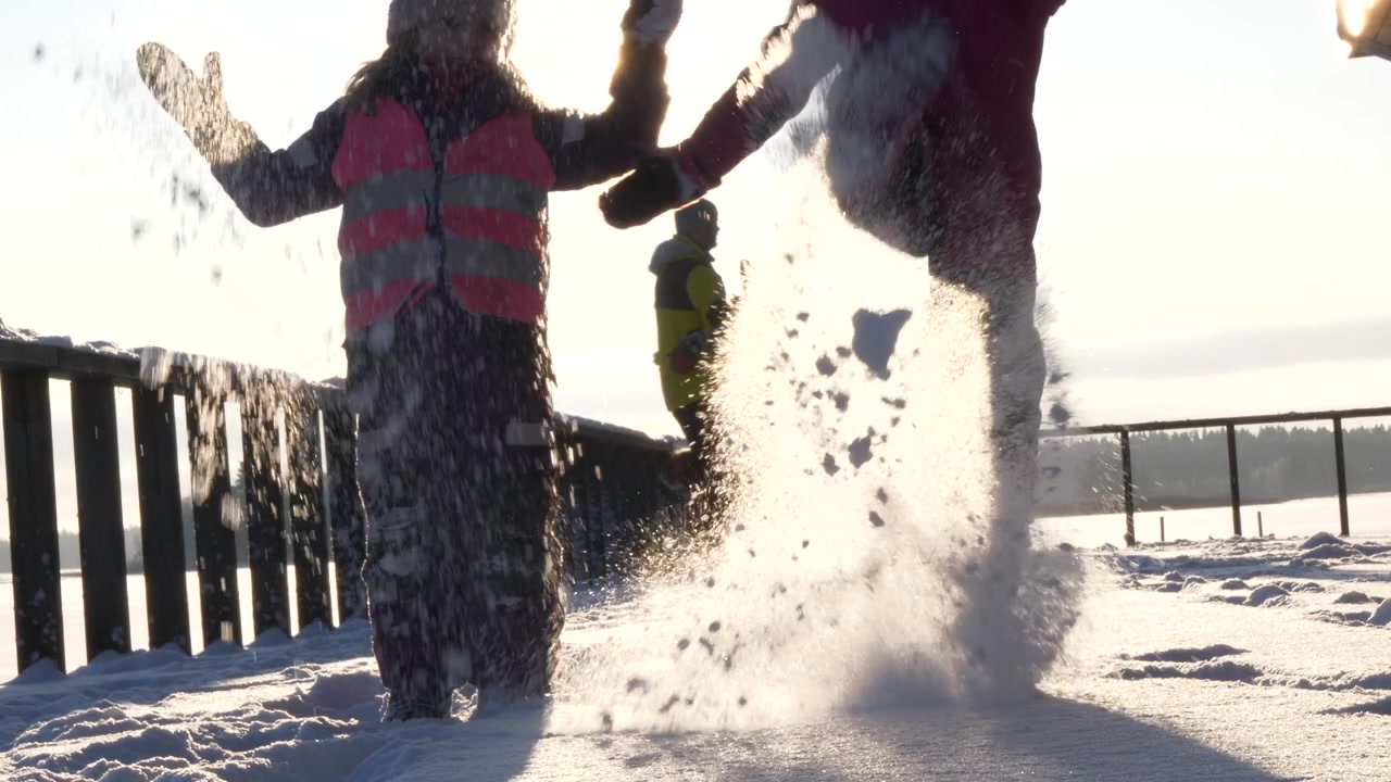 Untersicht: Zwei Kinder spielen im Schnee, Eltern im Hintergrund, sonniger Tag, statische Aufnahme
