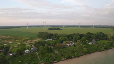 Drohne-Drängt-Auf-Eine-Gruppe-Von-Windmühlen-Auf-Einem-Feld-Hinter-Mehreren-Hütten-Am-Seeufer