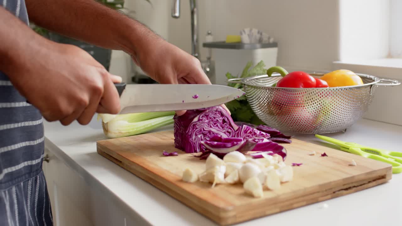 Close up of hands of biracial man in apron chopping vegetables in kitchen, slow motion