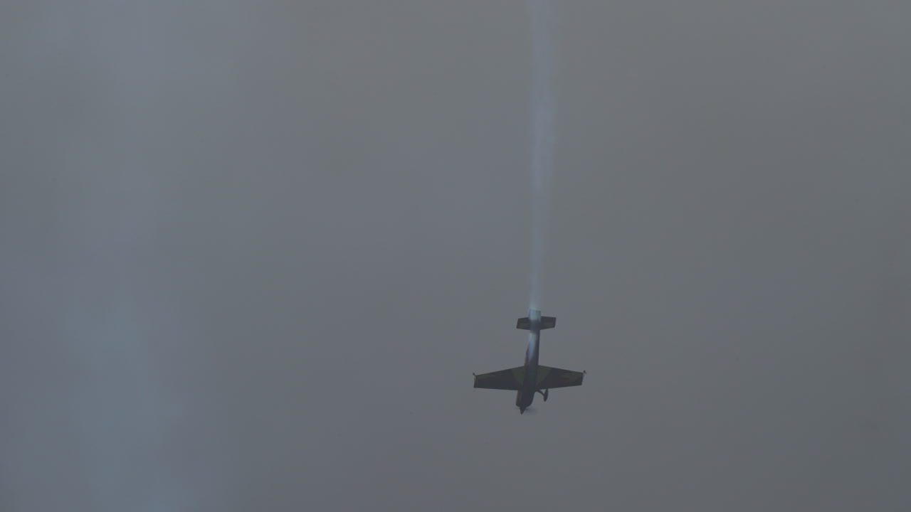 Aerobatic airplane performing a trick with imitation of falling down with black smoke trail against cloudy sky