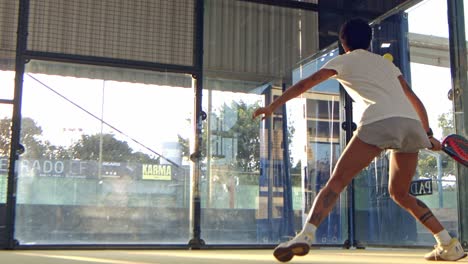 woman playing padel returns the ball off the back wall of the court