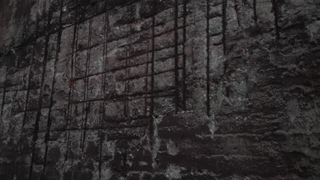 close-up, panning shot of a deteriorated concrete wall with exposed, rusty rebar, symbolizing decay and neglect