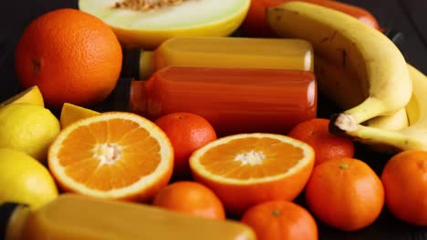 Mix-of-orange-and-yellow-colored-fruits-and-juices-on-black-wooden-background