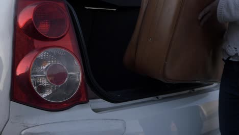 Woman-taking-old-brown-suitcase-out-of-car-boot-close-up-shot