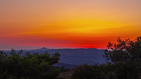 Timelapse-shot-of-sun-setting-in-the-background-over-a-mountain-range-covered-with-green-vegetation-during-evening-time