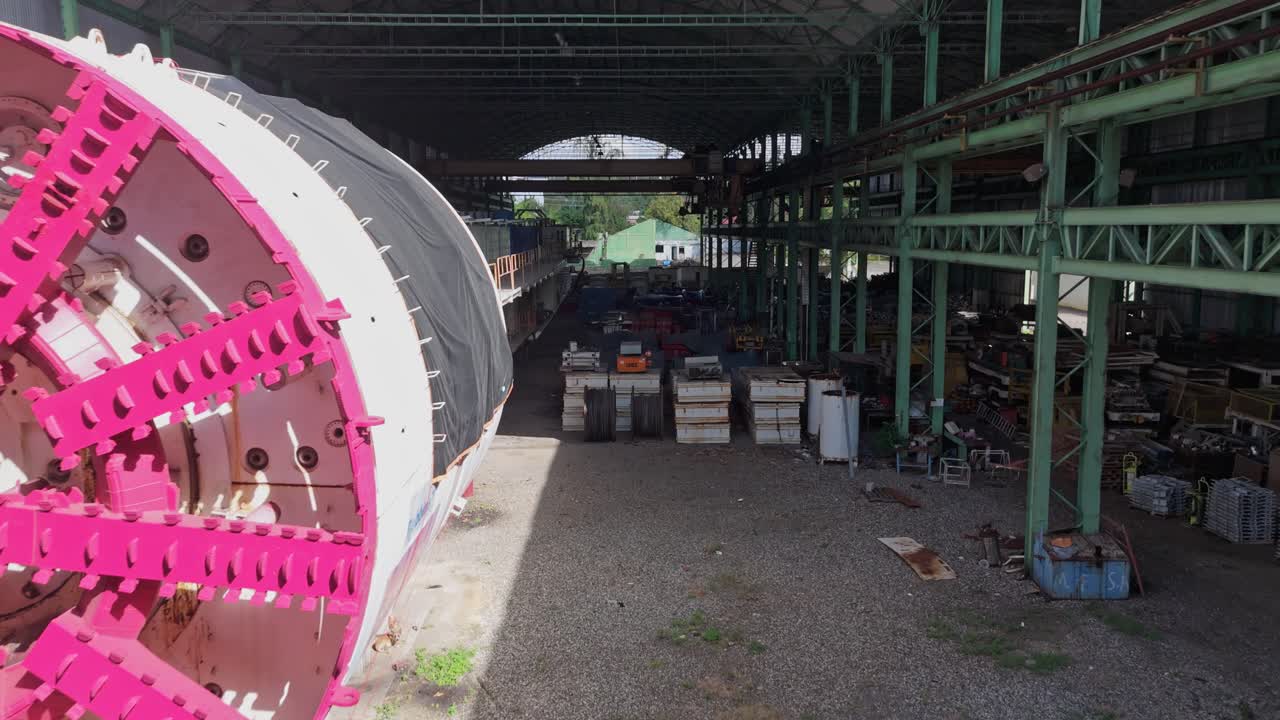 Underground tunnel boring machine (TBM) inside large industrial facility with various construction materials and heavy machinery. Drone