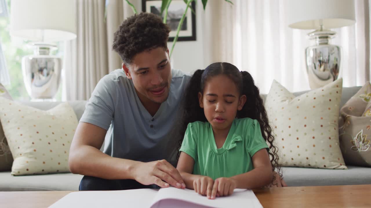 padre y hija biraciales felices sentados en el sofá leyendo braille