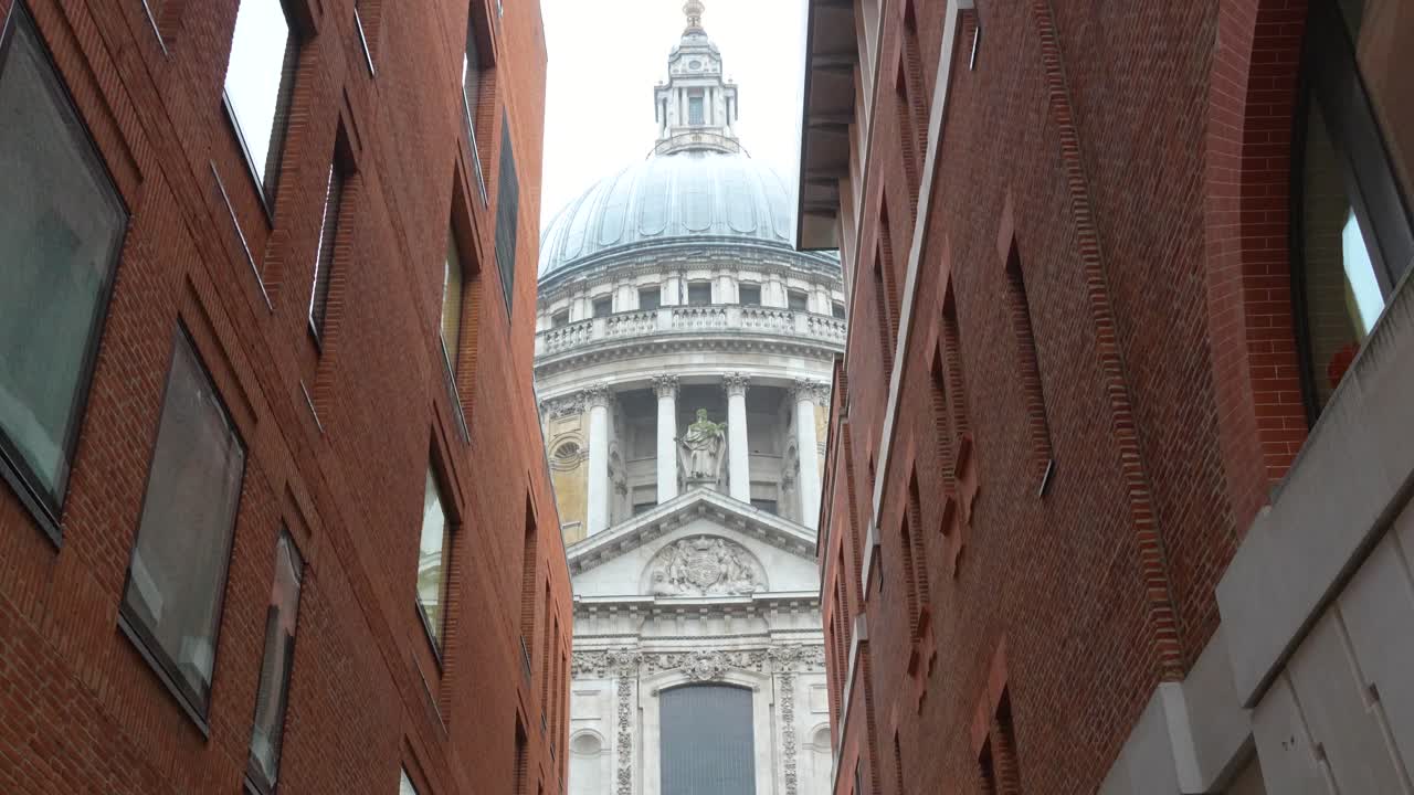 La cupola della Cattedrale di St Paul a Londra vista tra due edifici in una strada stretta. Vista diurna che mostra l'architettura della chiesa incorniciata dall'ambiente urbano