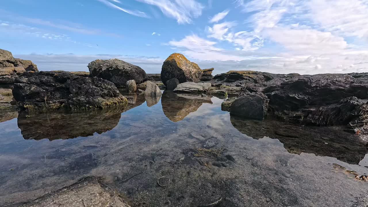 Mirrored reflection in clear sea water of beach boulder formation under perfect blue tropical sky