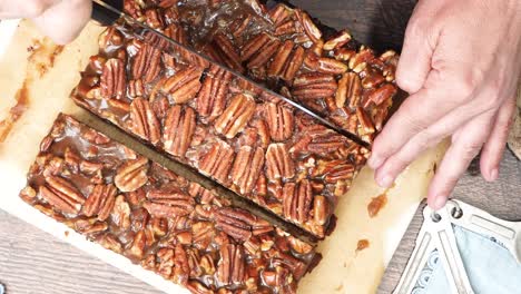 baking delicious caramel pecan brownies. using a knife to cut them into pieces on a wood cutting board. freshly baked gooey chocolate brownies with sweet caramel and nutty pecans.