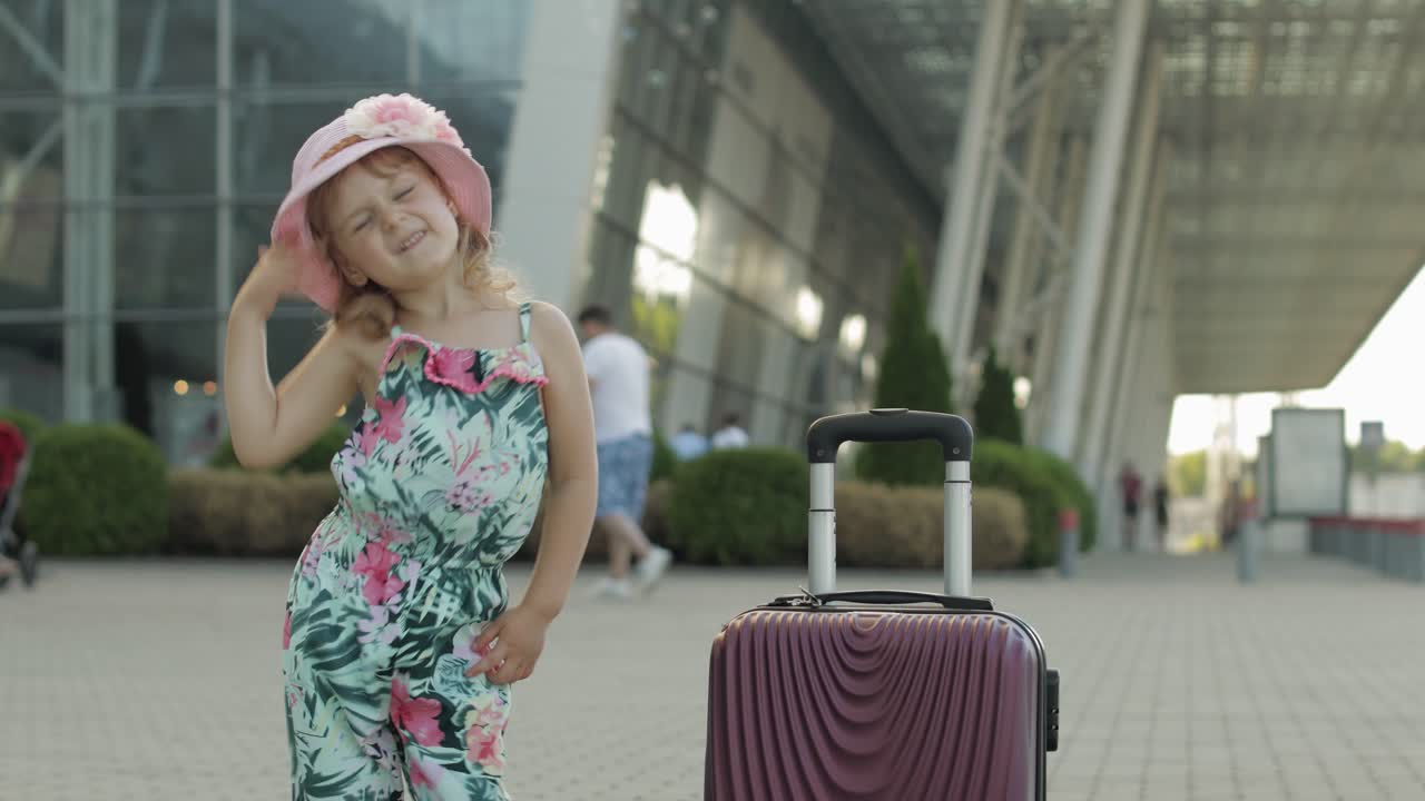 Menina turista com mala de viagem perto do aeroporto. A criança dança, se alegra, celebra.