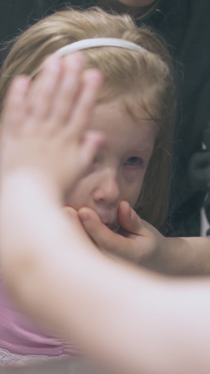 young mommy irrigates nose of blue eyed little girl with nasal spray at large mirror in bathroom at home