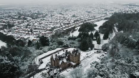 aerial view from behind belfast castle surrounded by snow, tilt up reveal