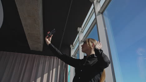 attractive woman holding a smartphone in front of herself. lady is posing in front of phone camera in a sunny office. view from below.