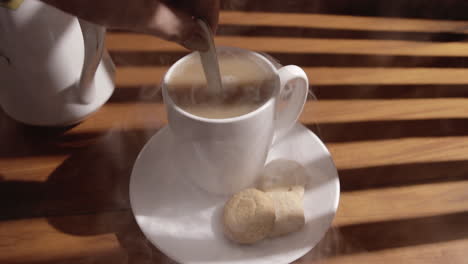 hand stirring steaming coffee in a cup on saucer with cookies