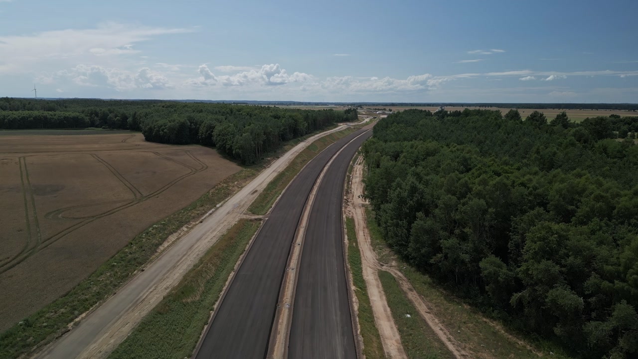 Aerial tracking over rural highway cutting through farmland toward Gdansk region, partial new build construction with sand and pavement