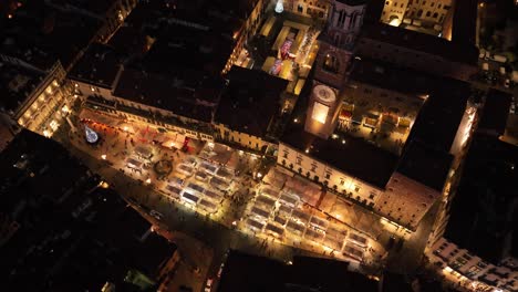 Vista-Aérea-Que-Gira-Hacia-Atrás-En-El-Sentido-De-Las-Agujas-Del-Reloj-De-La-Plaza-De-Erbe-Iluminada-Por-La-Noche---Verona