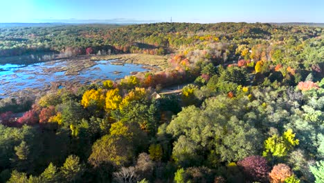 a breathtaking drone shot capturing a stunning sunset over a massachusetts lake in autumn. warm colors of the setting sun blend with the vibrant fall foliage, creating a serene and picturesque scene.