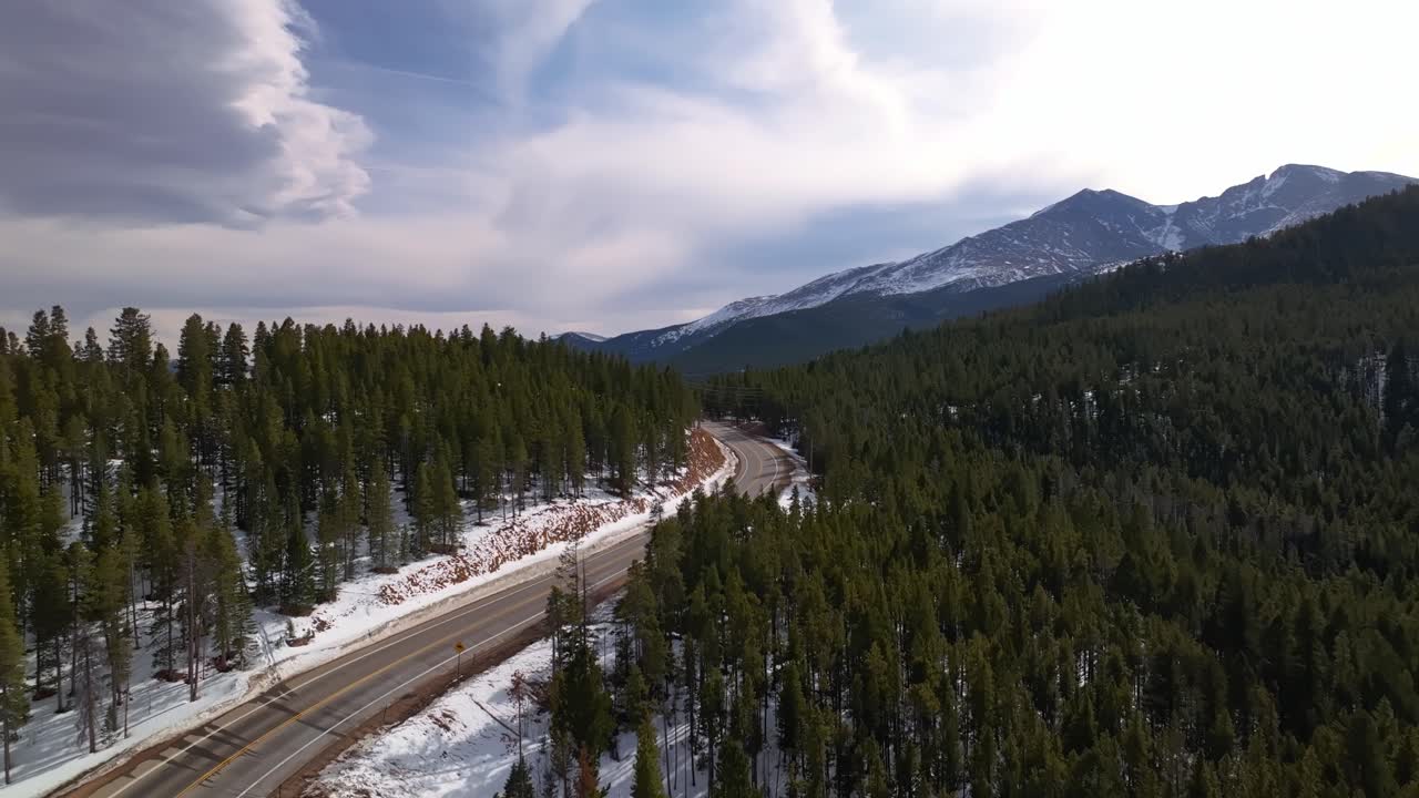 Aerial dolly over pine-lined mountain road in early spring with rocky ridges and distant peaks, Allenspark Colorado USA