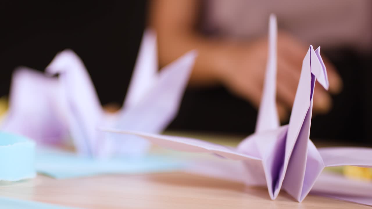 A detailed close up shot of a purple paper crane sitting on a wooden desk