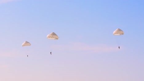 three paratroopers descending under white parachutes