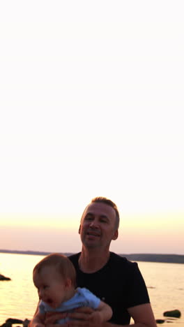 happy father and son playing cheerfully at the waterfront. dad is tossing his baby boy and he is laughing excitedly. river at backdrop. vertical video