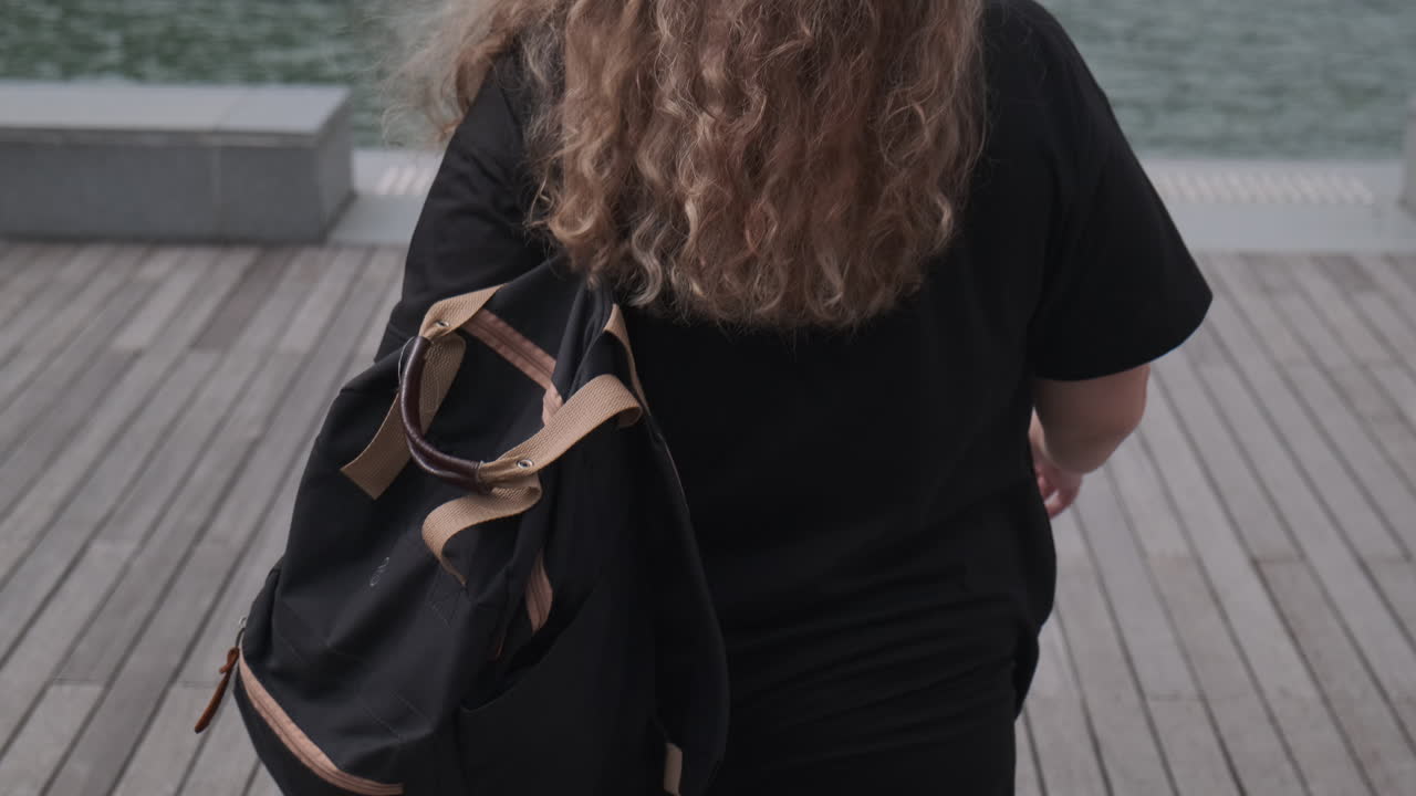 Woman with curly hair walking on a pier by the water