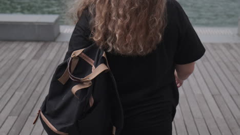 mujer con cabello rizado caminando en un muelle junto al agua