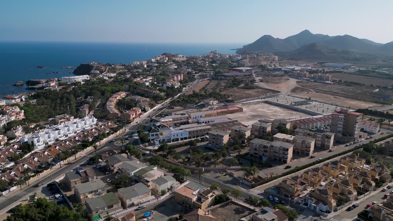 wide orbit aerial view of Cabo de Palos town or Cape Palos during a summer day in a small peninsula in the municipality of Cartagena, Murcia region - Mountains and mediterranean sea in the background.