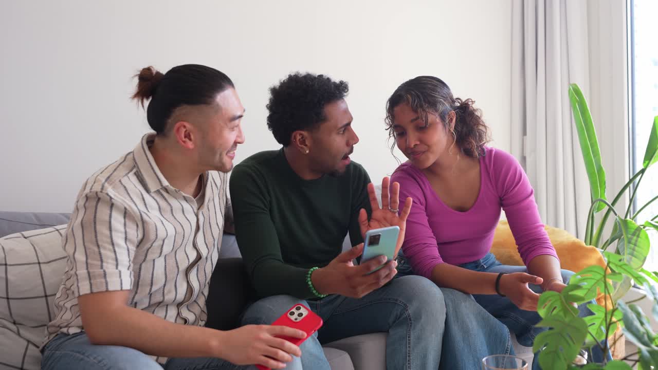 Happy Diverse Friends Laughing and Talking While Using Smartphones on Couch