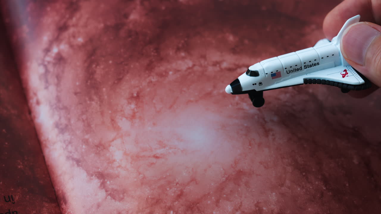 Close up of a miniature toy space shuttle placed on a reddish galaxy background