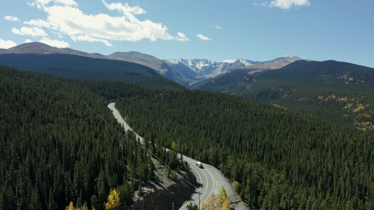 Ripresa aerea che segue un'autostrada forestale verde verso una catena montuosa in lontananza, 4K.