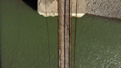 old suspension bridge over clear river water streaming, top down view