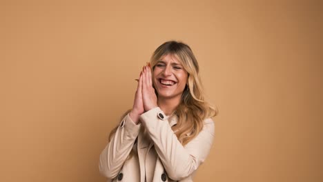 cheerful transgender woman in trench coat laughing against beige background