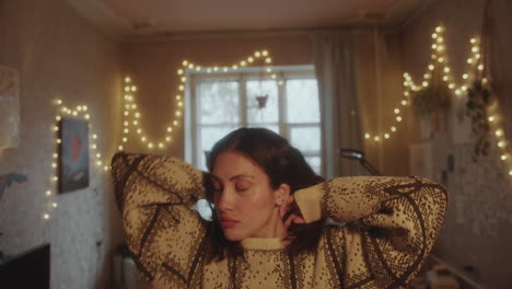 young sleepy woman twisting her hair and stretching arms in cozy room