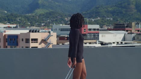 ascending camera movement of a young girl walking in high heels holding her luggage on a rooftop