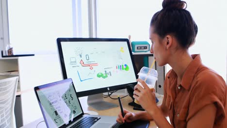 mujer ejecutiva trabajando en una tableta gráfica mientras toma jugo en su escritorio 4k